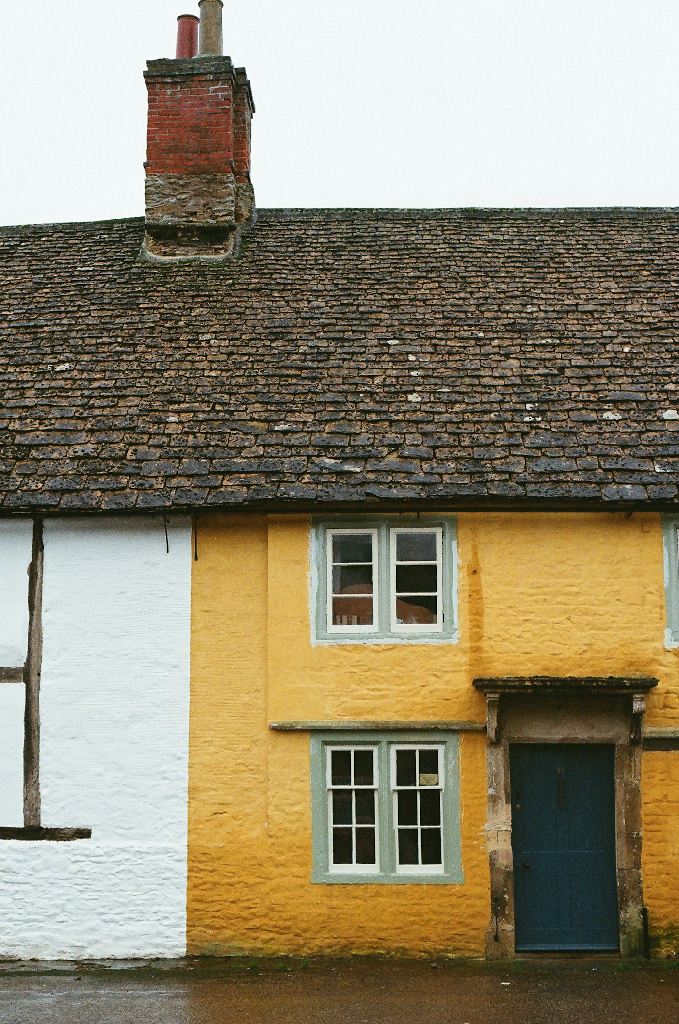Traditional English cottage with a tiled roof, yellow exterior and blue front door